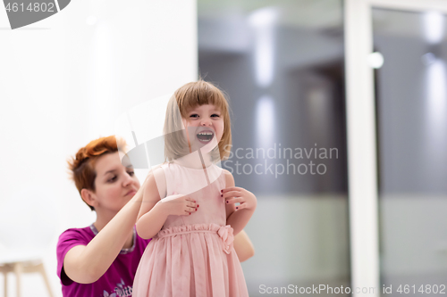 Image of young mother helping daughter while putting on a dress