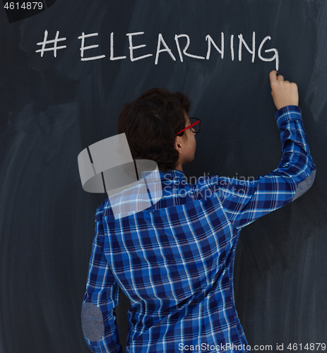 Image of Teen Boy with chalk  writing on black chalkboard hashtag elearni