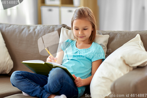 Image of little girl with diary sitting on sofa at home