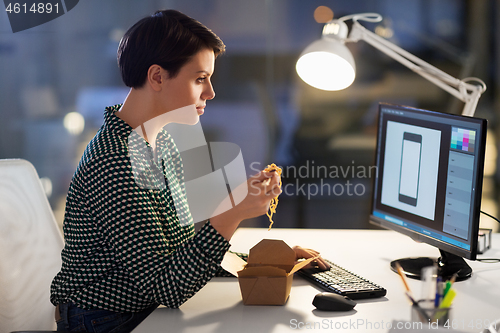 Image of female designer eating and working at night office