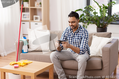 Image of man playing game on smartphone after cleaning home