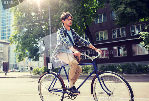 Image of young hipster man with bag riding fixed gear bike