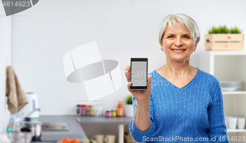 Image of smiling senior woman showing smartphone in kitchen