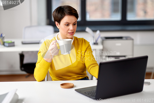 Image of businesswoman with laptop drinks coffee at office