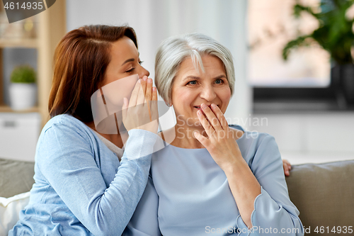 Image of adult daughter whispering to senior mother at home