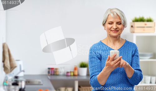 Image of smiling senior woman using smartphone in kitchen