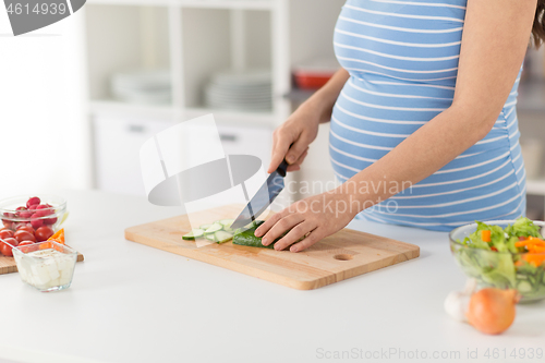 Image of pregnant woman cooking vegetable salad at home