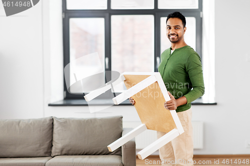 Image of happy indian man holding coffee table at home