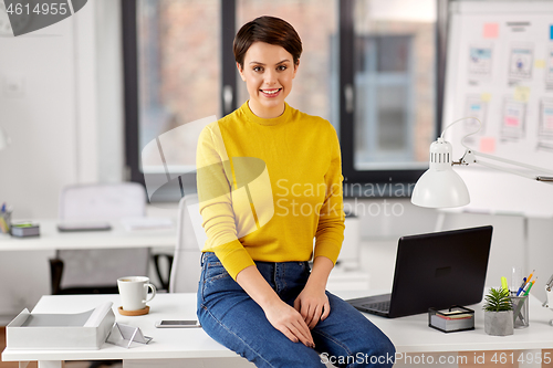 Image of happy businesswoman sitting on desk at office