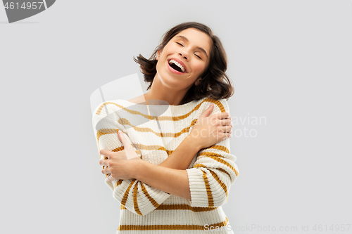 Image of happy woman in striped pullover hugging herself