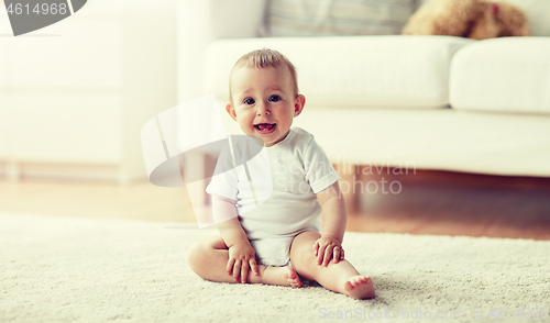 Image of happy baby boy or girl sitting on floor at home