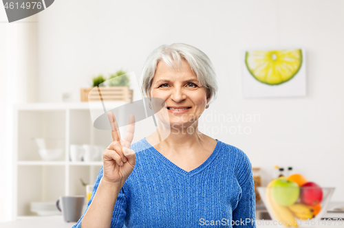 Image of smiling senior woman showing peace in kitchen