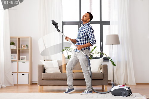 Image of indian man with vacuum cleaner having fun at home