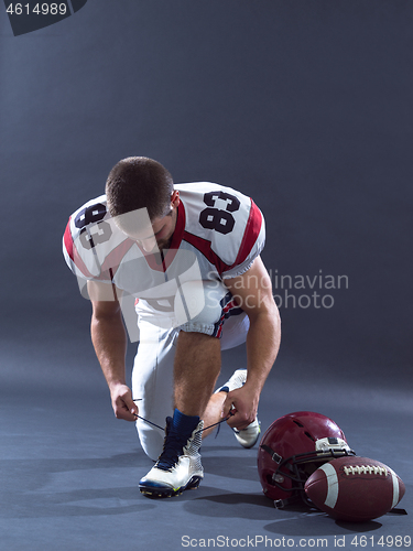 Image of American Football Player tie his shoe laces isolated on gray