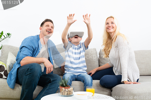 Image of Happy family at home on living room sofa having fun playing games using virtual reality headset