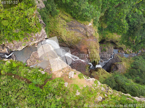 Image of Aerial top view of travel couple waving to drone, standing on the edge of 500 feet waterfall in the tropical island jungle of Black river gorges national park on Mauritius island