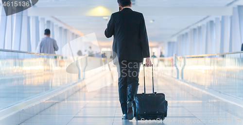 Image of Businessman walking and wheeling a trolley suitcase at the lobby, talking on a mobile phone. Business travel concept.