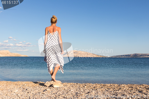 Image of Happy carefree woman enjoying late afternoon walk on white pabbled beach on Pag island, Croatia