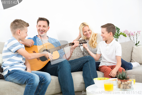 Image of Happy caucasian family smiling, playing guitar and singing songs together at cosy modern home