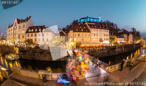 Image of View of lively river Ljubljanica bank in old city center decorated with Christmas lights at dusk. Old medieval Ljubljana cstle on the hill obove the city. Ljubljana, Slovenia, Europe