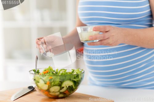 Image of close up of pregnant woman cooking salad at home