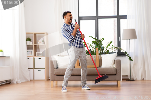 Image of man with broom cleaning and singing at home