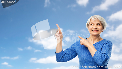 Image of smiling senior woman pointing fingers to sky