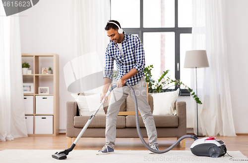 Image of man in headphones with vacuum cleaner at home