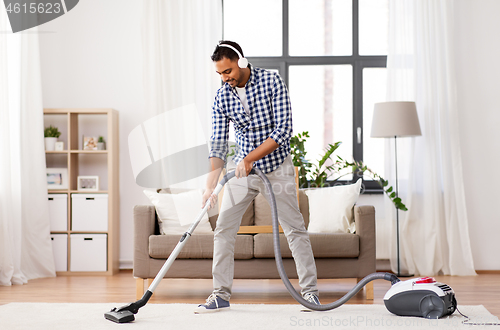 Image of man in headphones with vacuum cleaner at home