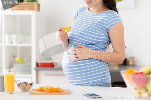 Image of close up of pregnant woman eating orange at home