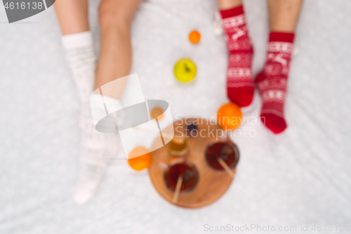 Image of Soft photo of woman and man on the bed with tea and fruits, top view point. Female and male legs in warm woolen socks