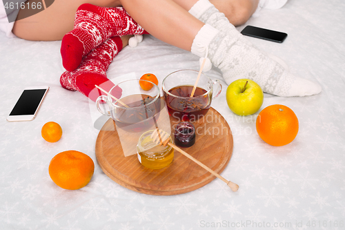 Image of Soft photo of woman and man on the bed with phone and fruits, top view point. Female and male legs in warm woolen socks