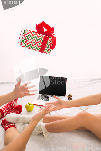 Image of caucasian couple at home with gift. Laptop and phone for people sitting on the floor