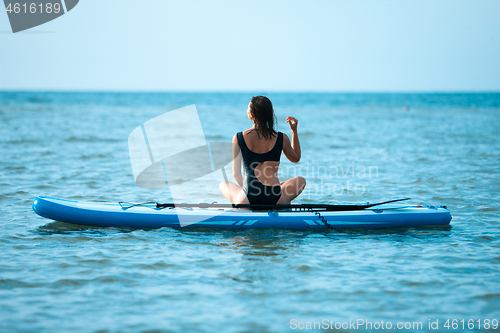 Image of Happy beautiful young girl with paddle board on beach. Blue sea in the background. Summer vacation concept.