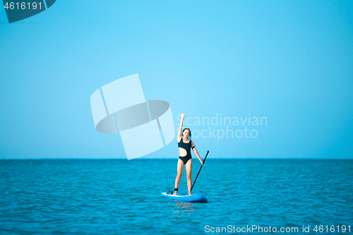 Image of Happy beautiful young girl with paddle board on beach. Blue sea in the background. Summer vacation concept.