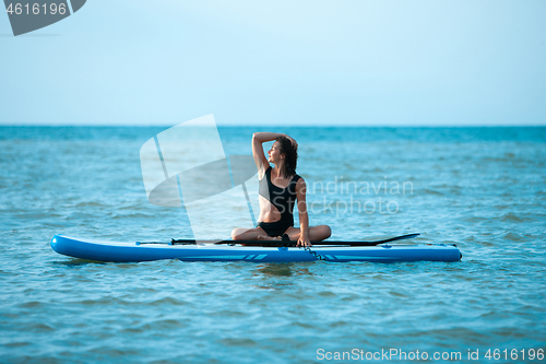 Image of Happy beautiful young girl with paddle board on beach. Blue sea in the background. Summer vacation concept.