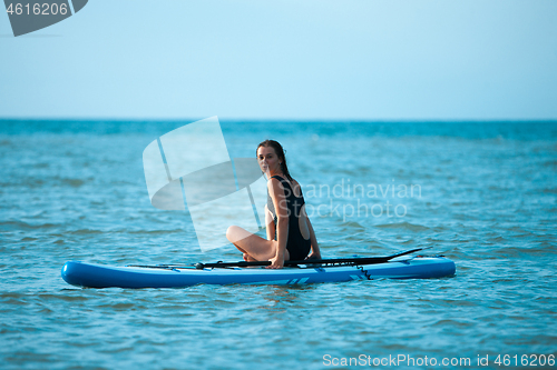 Image of Happy beautiful young girl with paddle board on beach. Blue sea in the background. Summer vacation concept.