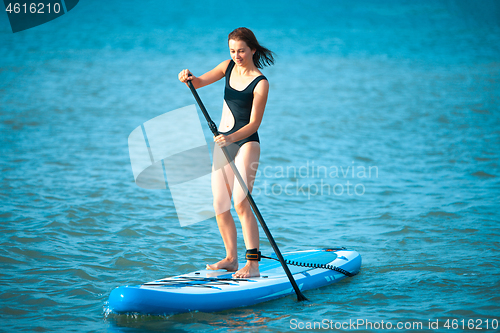 Image of Happy beautiful young girl with paddle board on beach. Blue sea in the background. Summer vacation concept.