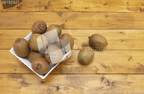 Image of White bowl full of fresh kiwis, with spilled fruits