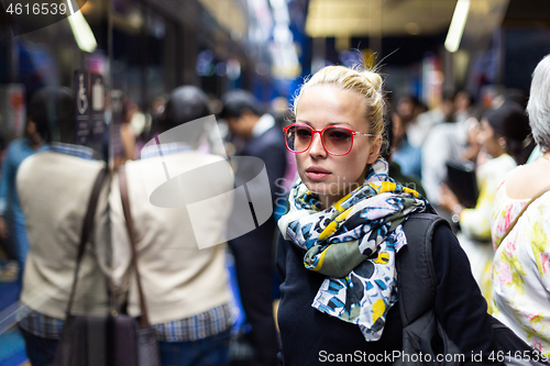 Image of Young woman wearing colorful scarf waiting on the platform of a urban metro station for train to arrive. Public transport