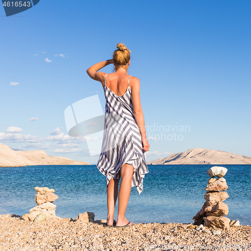 Image of Happy carefree woman enjoying late afternoon walk on white pabbled beach on Pag island, Croatia