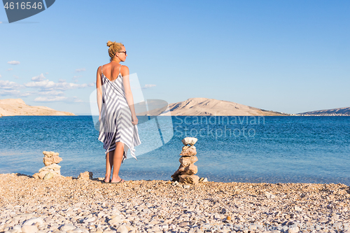 Image of Happy carefree woman enjoying late afternoon walk on white pabbled beach on Pag island, Croatia