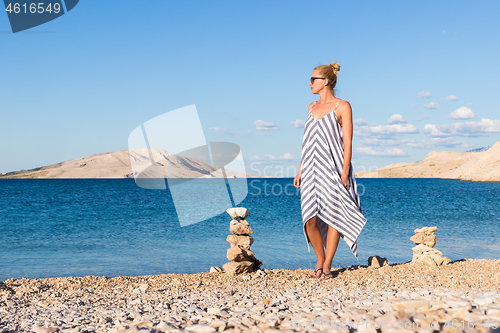 Image of Happy carefree woman enjoying late afternoon walk on white pabbled beach on Pag island, Croatia