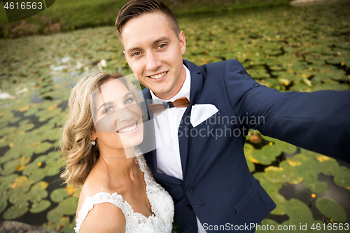 Image of Wedding selfie. Bride and groom hugging tenderly posing during photo shooting in park.