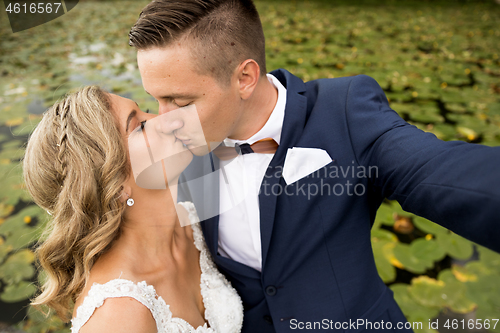 Image of Wedding selfie. Bride and groom kissing passionately outdooors in park.