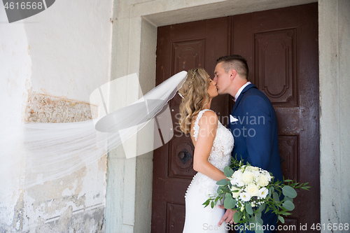 Image of The Kiss. Bride and groom kisses tenderly in front of church portal.