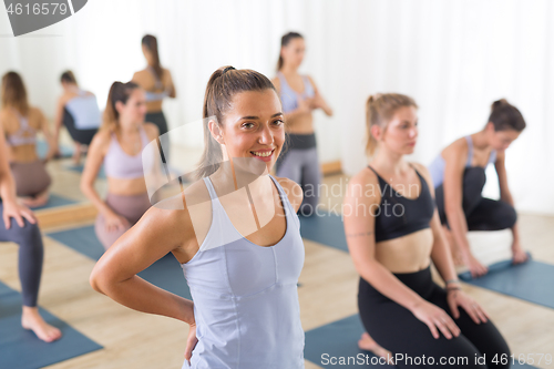 Image of Portrait of a cheerful beautiful young yoga instructor relaxing after giving yoga class to large group of sporty attractive people. Healthy active lifestyle, working out indoors in gym.