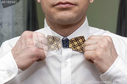 Image of A man in white shirt straightens wooden bow tie in a rustic style
