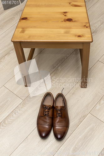 Image of Classic men&#39;s shoes with laces near wooden chair on wooden floor, vertical