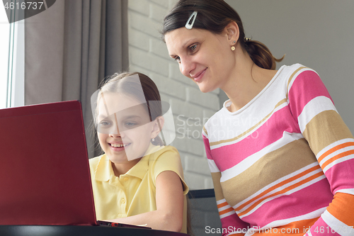 Image of Happy girl and girl are sitting at the table and looking at the laptop screen.